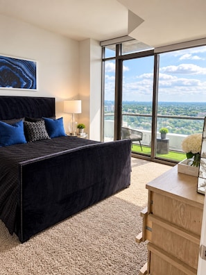 A modern bedroom with a large bed, a desk, and a view of a cityscape through large windows. - Luxury skyline living (Atlanta)