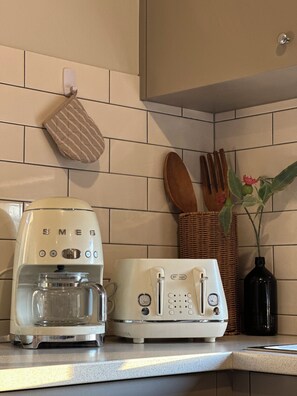 Eine Küche mit einer weißen Kaffeemaschine, einem Toaster, einem Korbkörbchen mit Besteck und einer Pflanze in einer Vase.