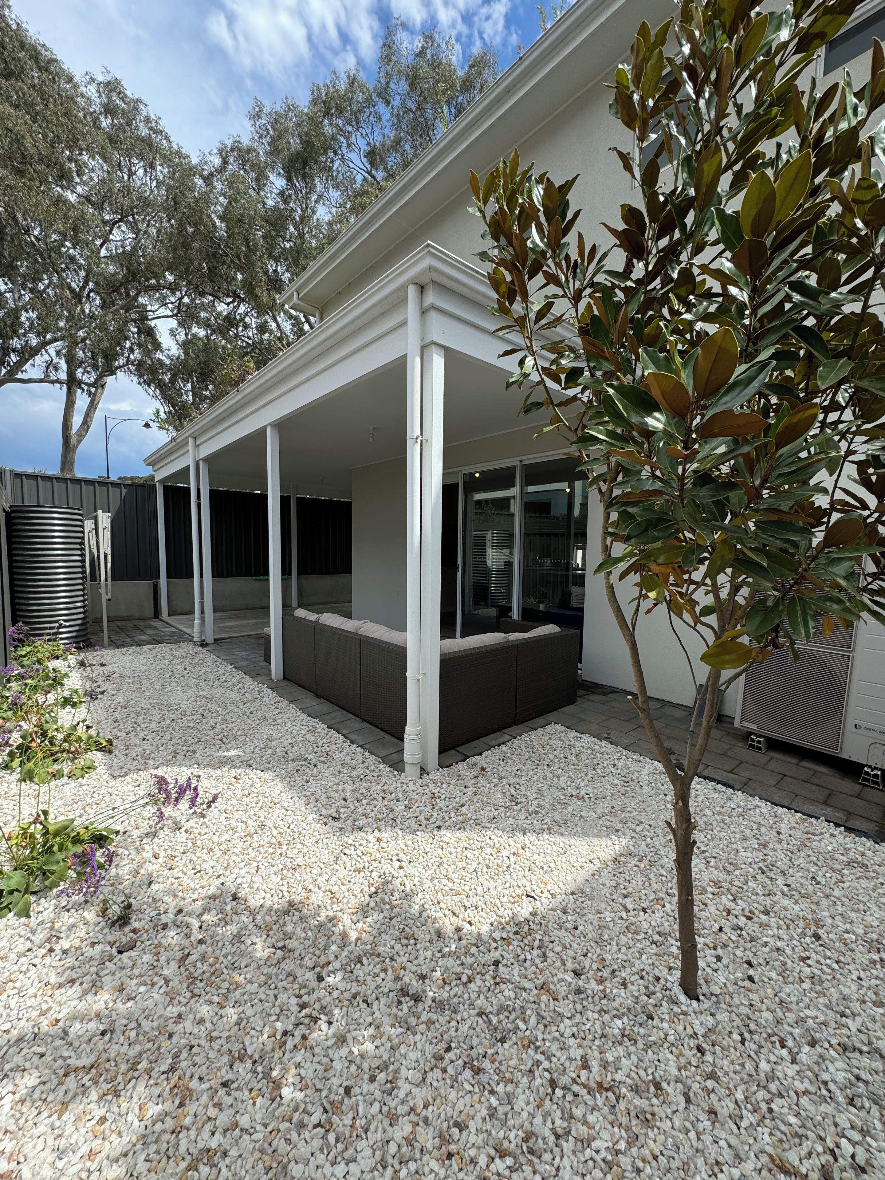 A covered outdoor seating area with a white structure, surrounded by gravel and a small tree.