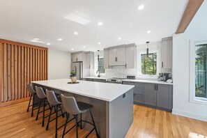 A modern kitchen with a large island, bar stools, and a wooden slat wall.