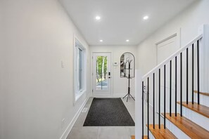 A hallway with a dark rug, white walls, a coat rack, and a staircase with wooden steps and black railings.