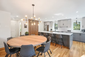 A modern kitchen with a central island, grey cabinetry, and a wooden dining table with chairs.