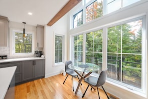 A modern kitchen with large windows, a dining area with a glass table, and wooden flooring.
