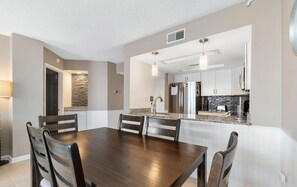 A modern kitchen with stainless steel appliances, a stone backsplash, and a dining area with a wooden table and chairs. - Nautilus Heights - St. Regis Condo #3110 (North Topsail Beach)
