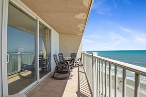 A balcony with a view of the ocean, a table with chairs, and a glass door leading to an interior space. - Ocean Front Paradise - St. Regis Condo #1407 (North Topsail Beach)