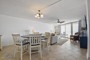 A spacious living area with a dining table, chairs, a sofa, and a ceiling fan. - Ocean Front Paradise - St. Regis Condo #1407 (North Topsail Beach)