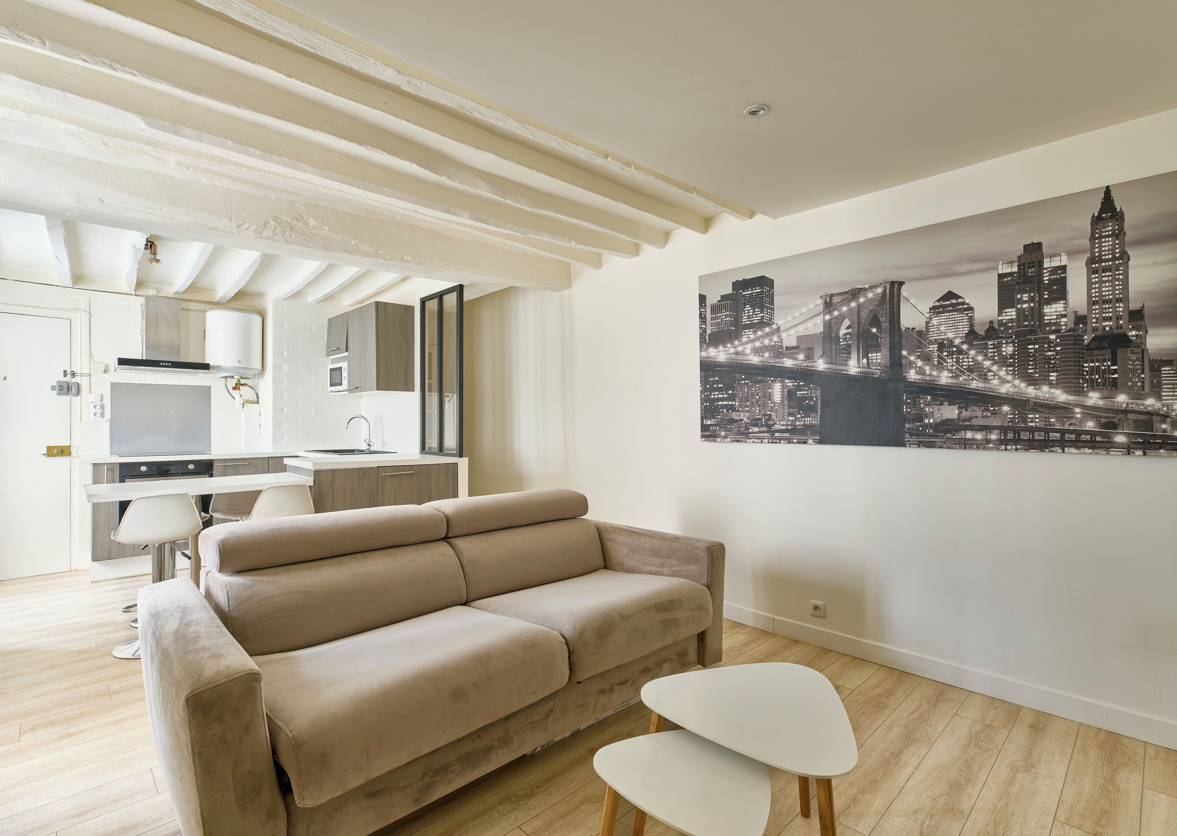 Een moderne woonkamer met een beige bank, een witte salontafel en een stadslandschap schilderij aan de muur.