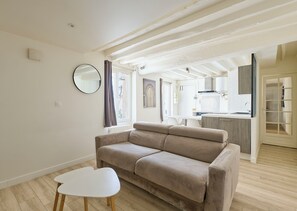 Ein modernes Wohnzimmer mit einem beigen Sofa, einem weißen Couchtisch und einer Küche im Hintergrund.