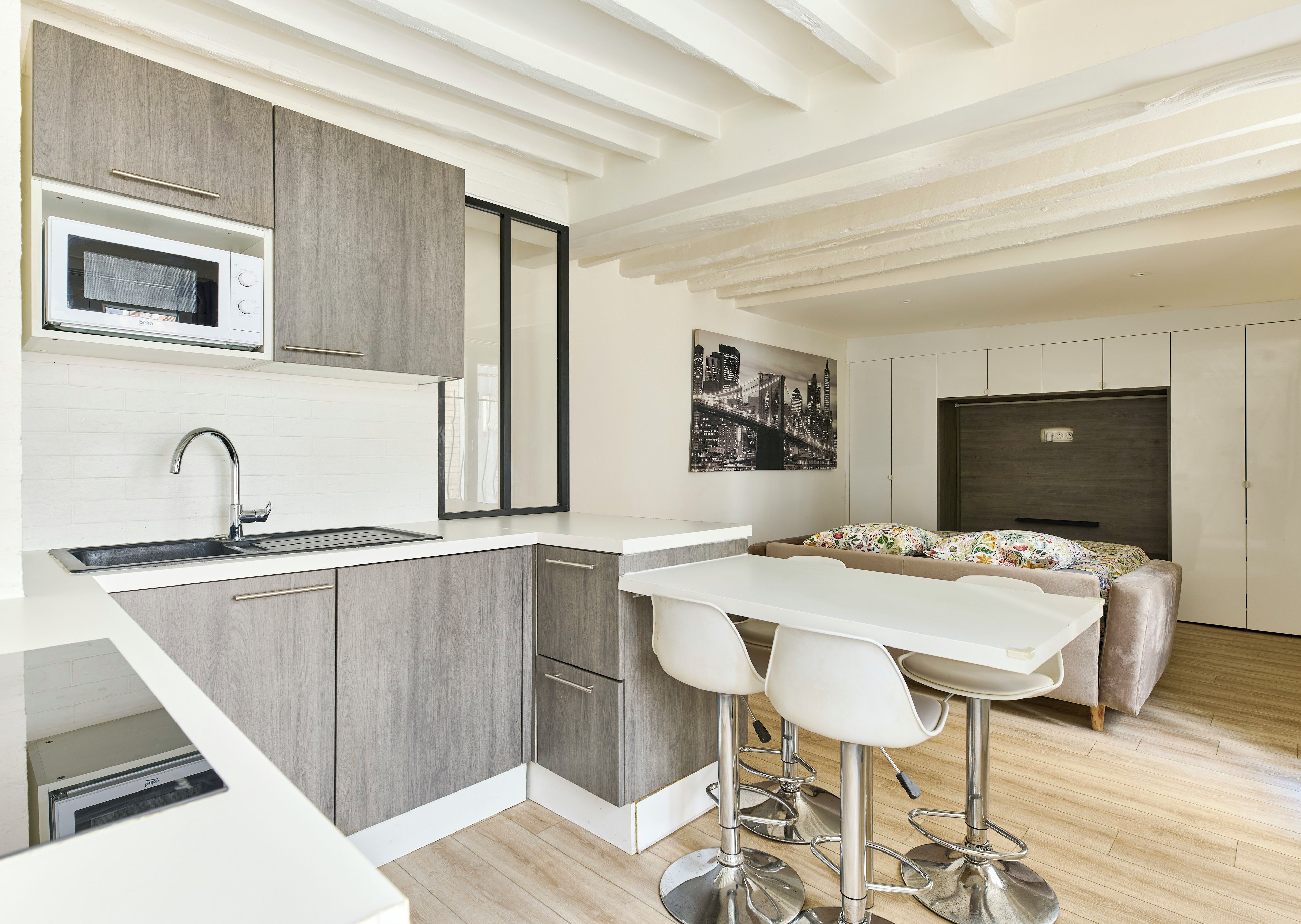 Een moderne keuken met een inbouwmagnetron, een spoelbak en een eethoek met barstoelen.