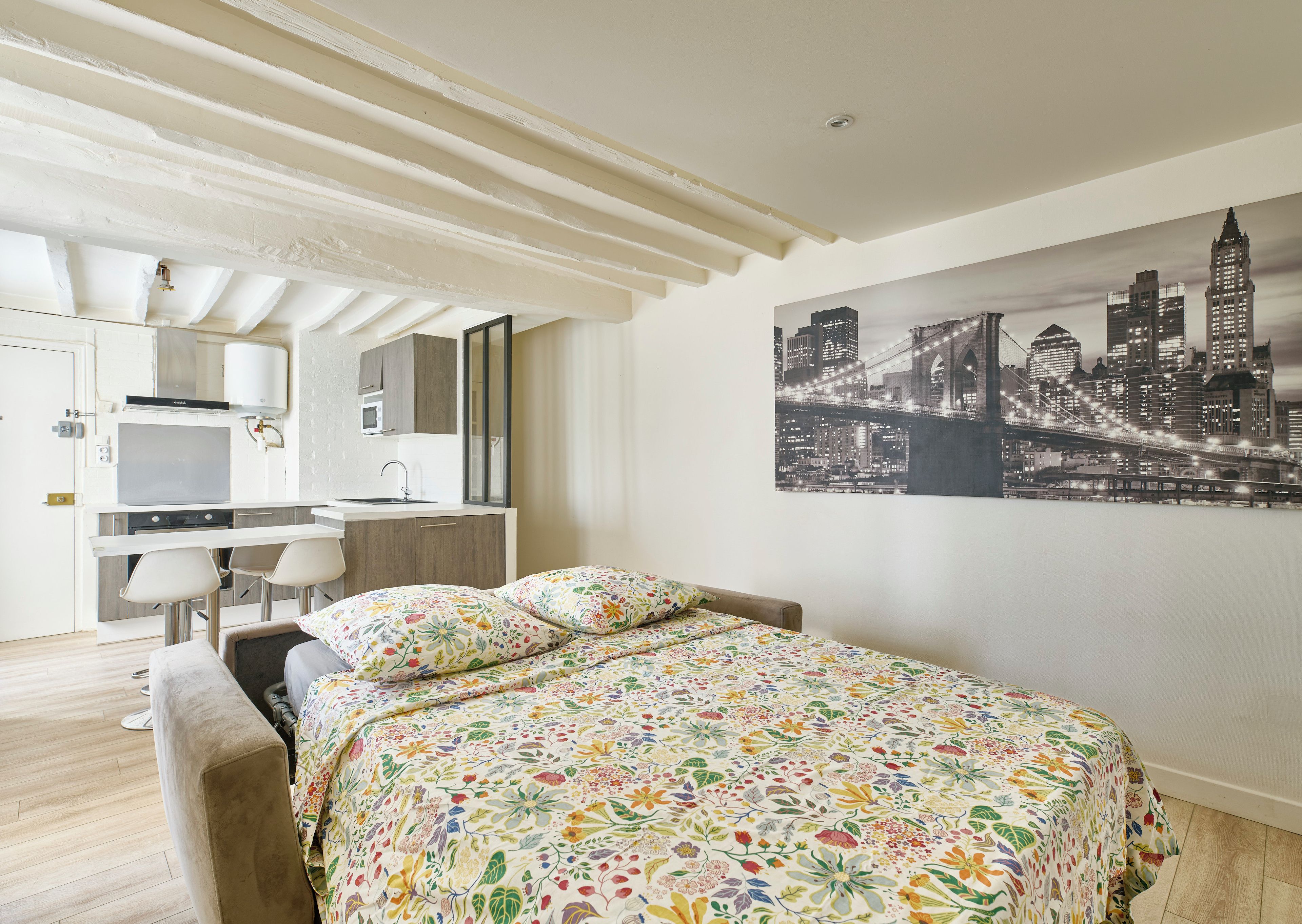 Een moderne slaapkamer met een bed, stadsgezicht kunst aan de muur, een kitchenette en een badkamer.