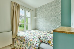 Une chambre à coucher avec un lit, une fenêtre avec des rideaux, un papier peint à motifs et un interrupteur sur le mur.