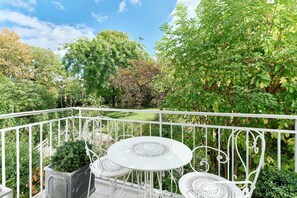 Un balcon doté d’une balustrade en métal blanc, d’une table ronde et de deux chaises.