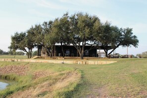 A rustic building with a stone facade, surrounded by mature trees and a grassy field. - Charming 2-bedroom cabin located on a private ranch near Devine/Moore with views (Moore)