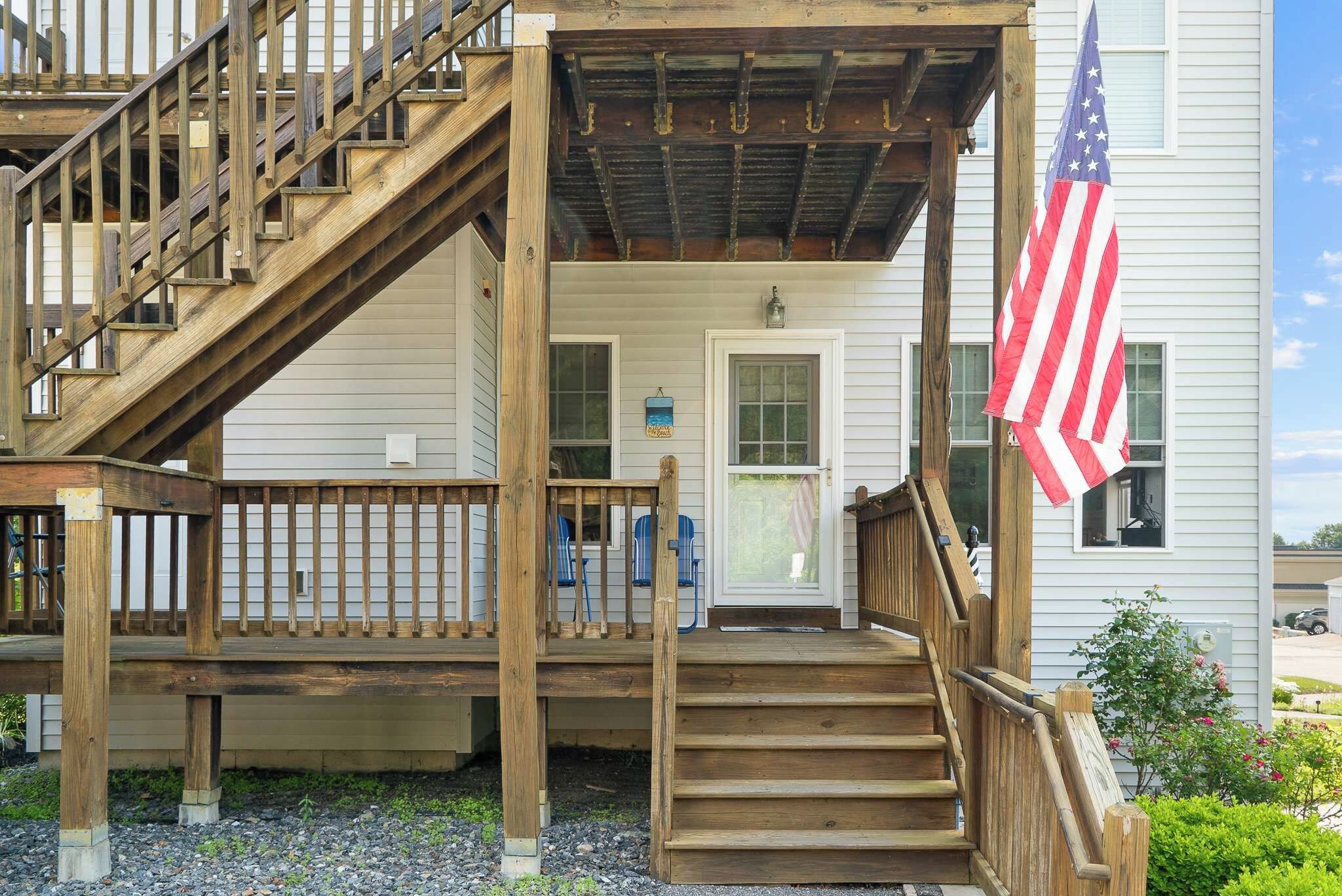 A wooden staircase leading to a porch with a railing, a door, and an American flag.