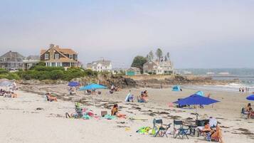 A beach with people, umbrellas, and houses in the background.