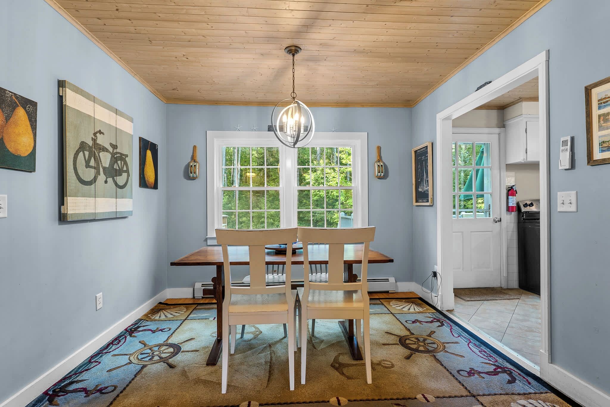 A dining area with a wooden table and chairs, a chandelier, and a window with a view of greenery.