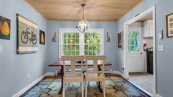 A dining area with a wooden table and chairs, a chandelier, and a window with a view of greenery.
