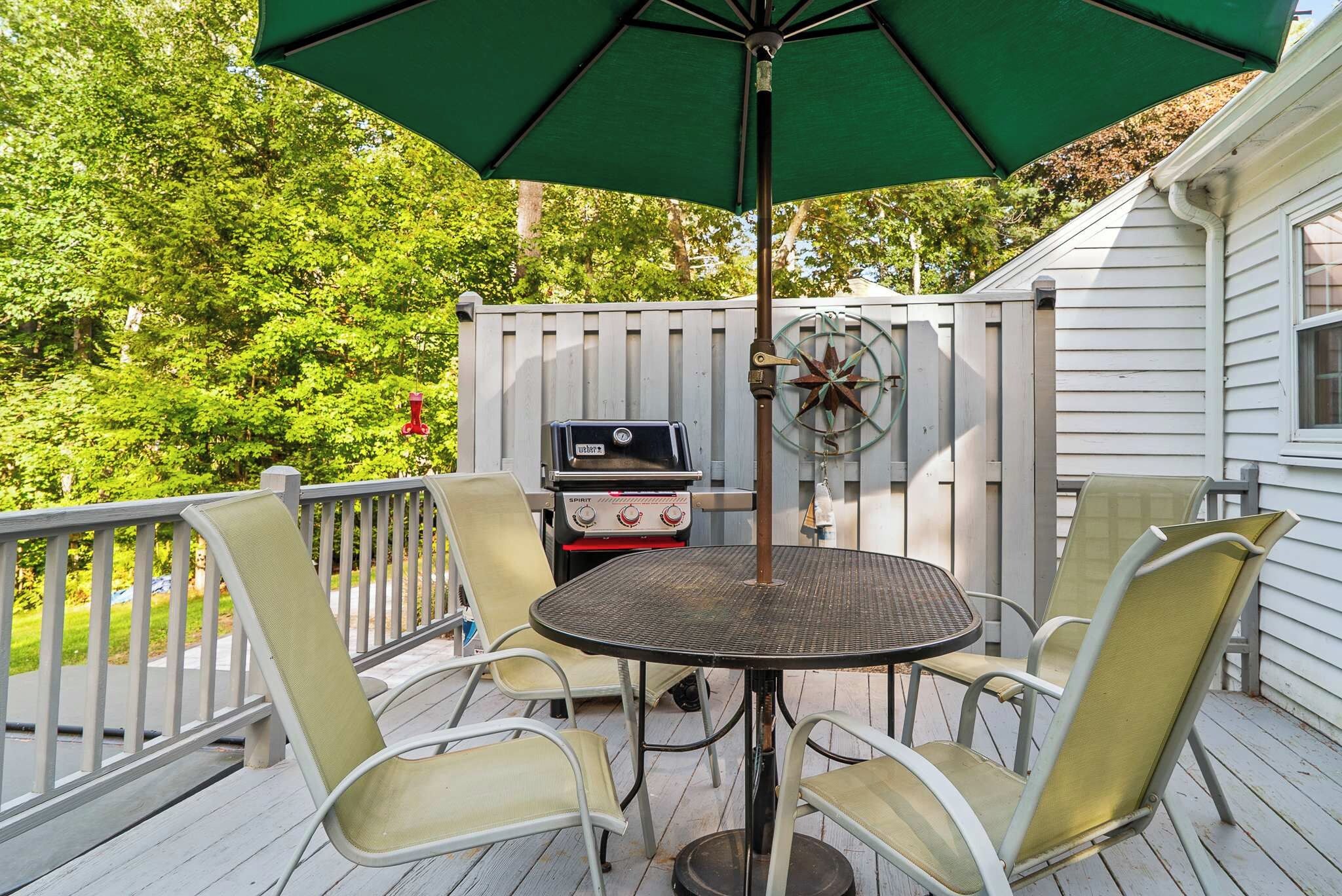 A deck with a table and chairs, a grill, and an umbrella.