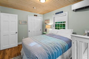 Une chambre à coucher comprenant un lit, une table de chevet, une lampe, une fenêtre et une porte portant l’inscription « DOCK SQUARE ».
