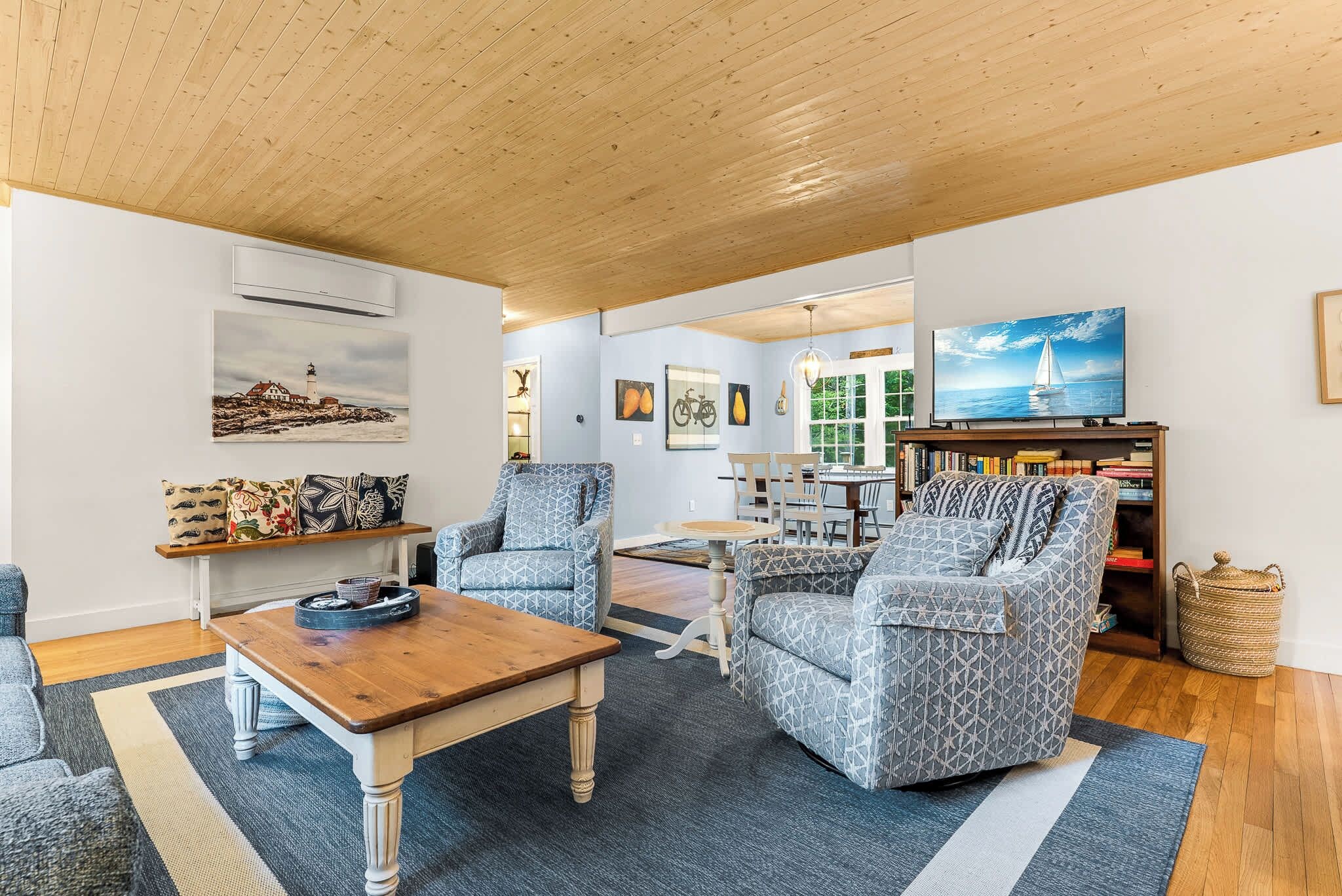 A spacious living room with a wooden ceiling, a television, a bookshelf, and a dining area with chairs and a table.
