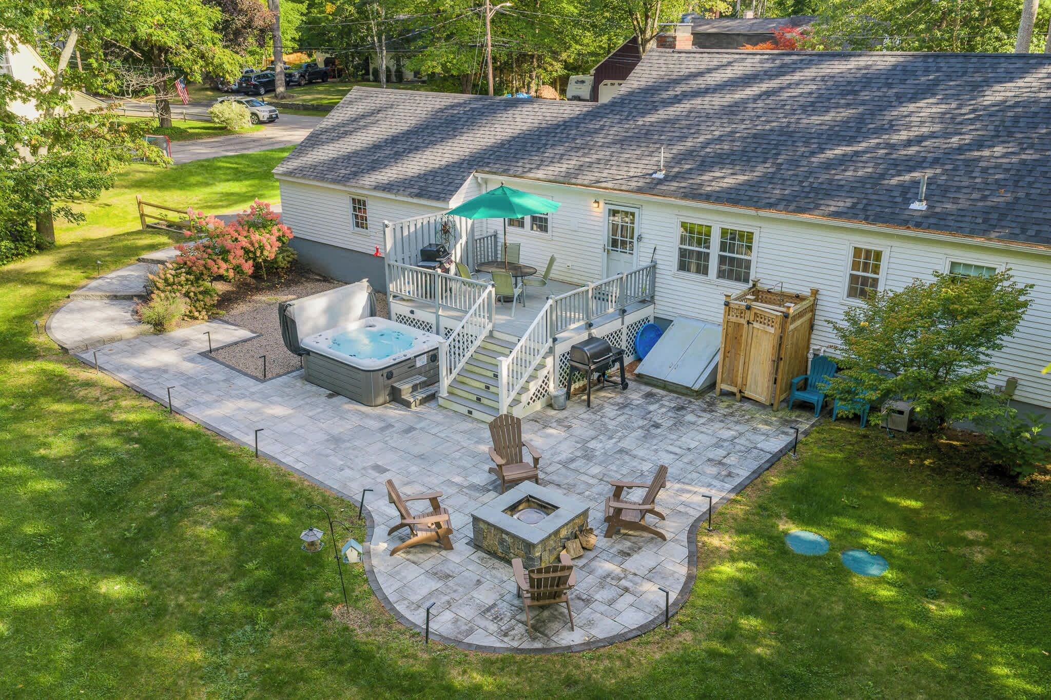 A residential backyard with a hot tub, outdoor seating, a fire pit, and a covered patio area.