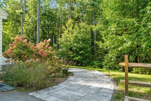 Un sentier de pierres traverse une zone boisée, et un banc en bois se trouve sur la droite.