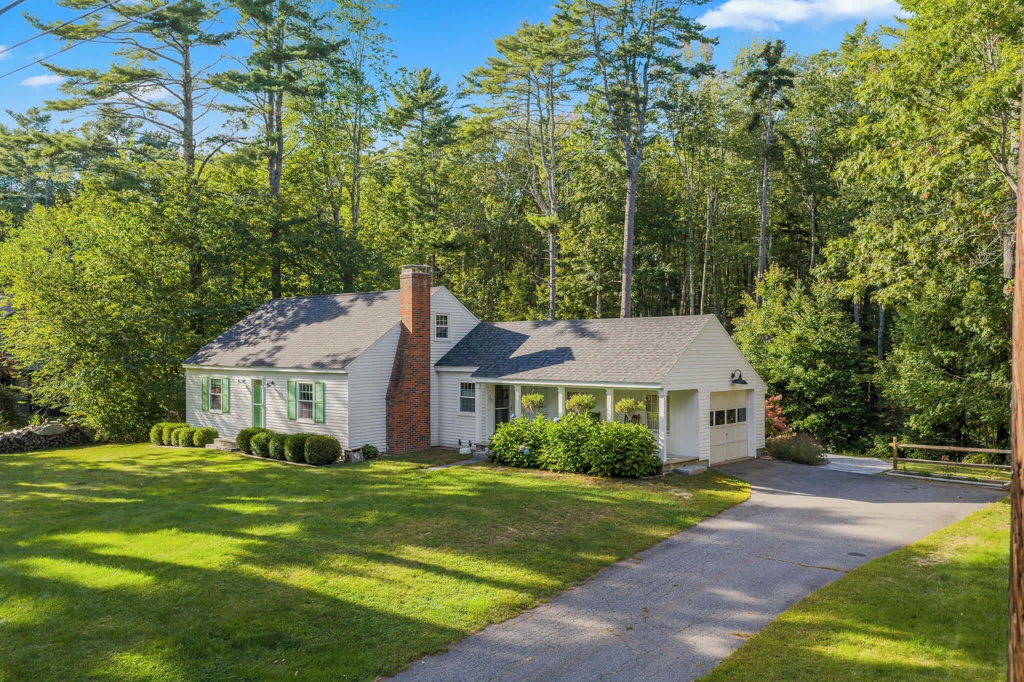 A single-story house with a chimney, surrounded by a well-maintained lawn and dense trees.