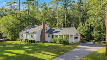 A single-story house with a chimney, surrounded by a well-maintained lawn and dense trees.