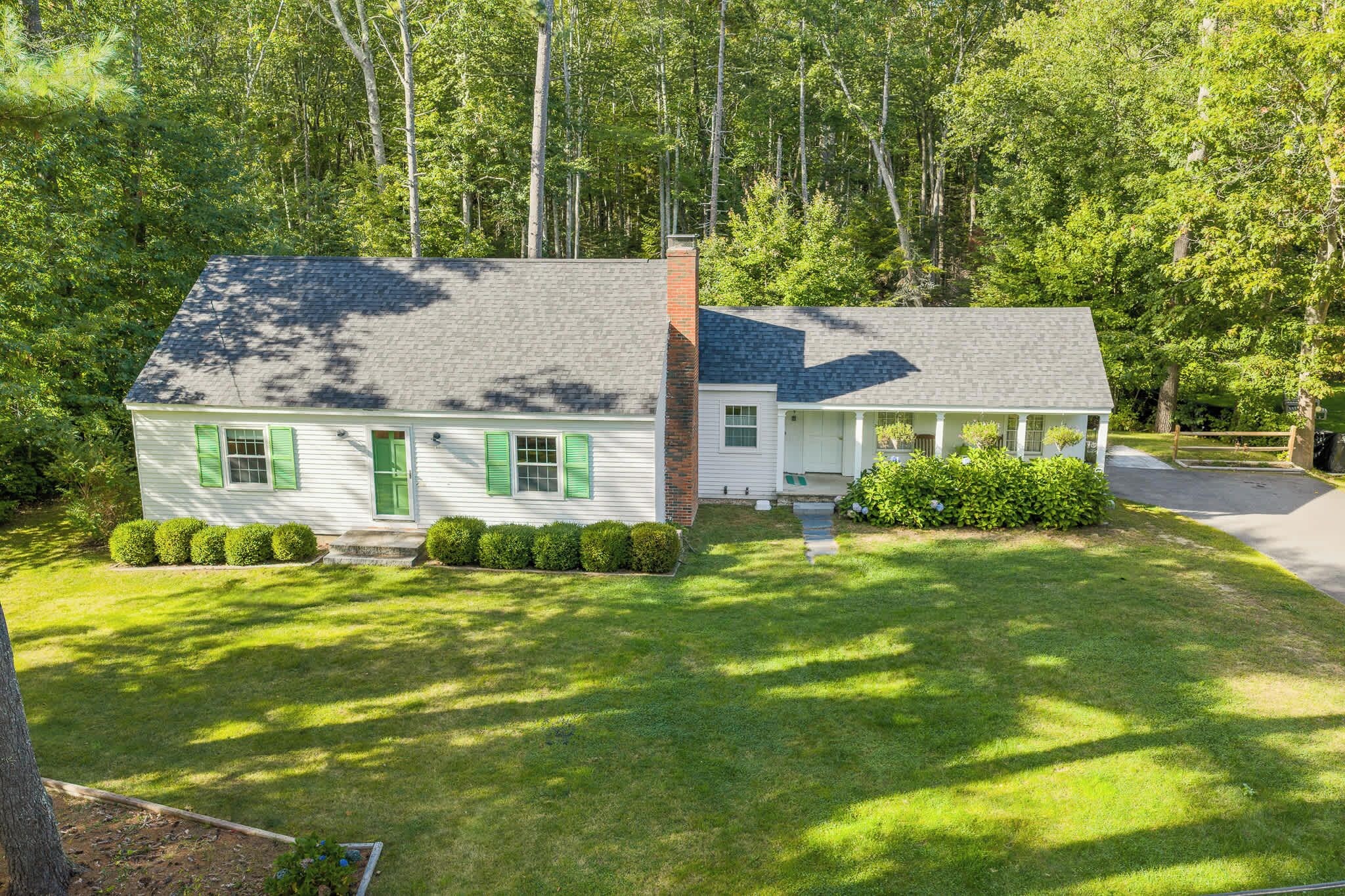 A two-story house with a front porch, surrounded by a well-maintained lawn and dense trees.