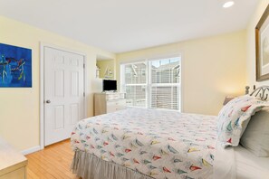A bedroom with a bed, a door, a window with blinds, a TV, and a painting on the wall. - Salty Breeze Condo with Pool (Wells)