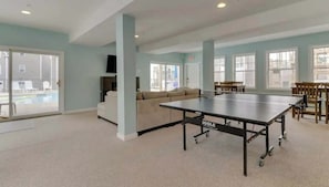 A spacious room with a ping pong table, a sofa, and a large window. - Salty Breeze Condo with Pool (Wells)