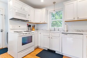 A modern kitchen with white cabinetry, a built-in oven, a dishwasher, and a window with blinds. - Salty Breeze Condo with Pool (Wells)