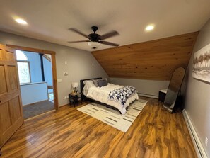 A bedroom with a bed, a ceiling fan, a nightstand, a lamp, a radiator, and a window. - Secluded VT Mountain Retreat - Scenic Views Near Stowe, Smugs & Jay Peak (Hyde Park)