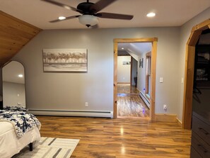 A bedroom with a bed, a ceiling fan, a painting, and a hallway leading to another room. - Secluded VT Mountain Retreat - Scenic Views Near Stowe, Smugs & Jay Peak (Hyde Park)