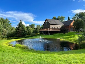 A house with a large deck, a pond, and a well-maintained lawn. - Secluded VT Mountain Retreat - Scenic Views Near Stowe, Smugs & Jay Peak (Hyde Park)