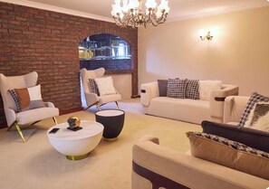 A living room with a brick wall, two white sofas, a round coffee table, and a chandelier. - 5 BRD| sleeps 10| near airport|Perth CBD| Kings Park| mint (Dianella)