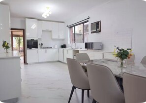 Une cuisine moderne avec des meubles blancs, un coin repas doté d’une table en marbre et une petite fenêtre offrant une vue agréable.