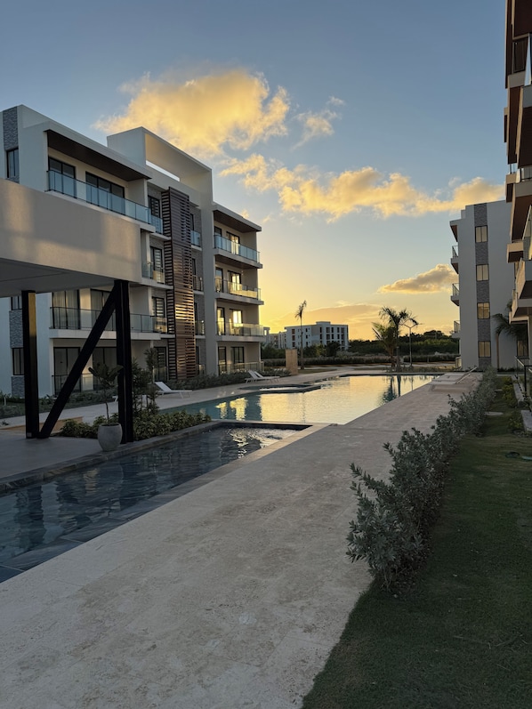 Un immeuble résidentiel moderne doté de nombreux balcons, d’une piscine et offrant une vue sur un ciel dégagé.