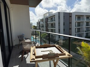 A balcony with a wooden table and chairs, overlooking a swimming pool and modern buildings. - Your Oasis in Punta Cana: 2-Bedroom Apartment for 6 People with a Pool (Punta Cana)