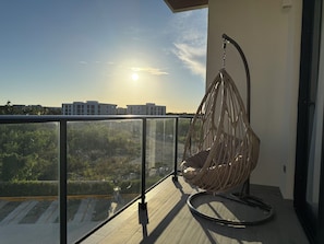 Ein Balkon mit einer Hängematte, einer Glastrennwand und Blick auf Gebäude und Grünflächen.