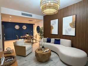 Ein modernes Wohnzimmer mit einer gebogenen Couch, einem runden Couchtisch und einem Essbereich mit blauer Akzentwand und Wanduhren.