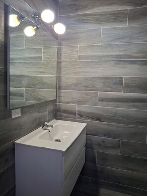 A bathroom with a white sink, a mirror, and a wall with grey tiles. - 2 Walking to the beach (Noord)
