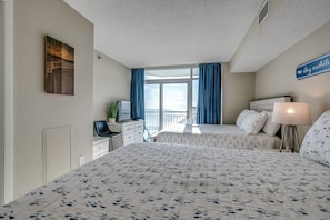 A hotel room with two beds, a desk with a computer, a TV, and a window with curtains. - Penthouse Paradise, Oceanfront Corner 2BD/2BA w/Panoramic Views, Prime location. (Myrtle Beach)