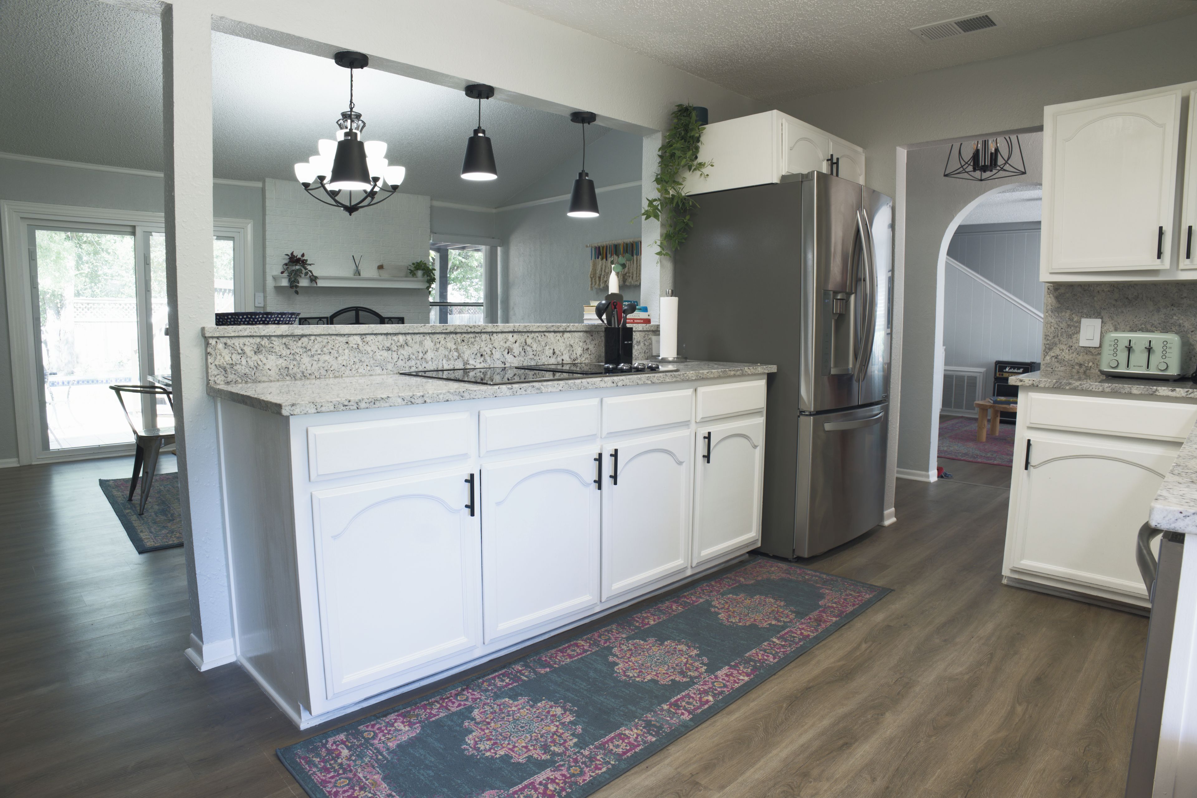 A modern kitchen with white cabinetry, a stainless steel refrigerator, and pendant lighting.