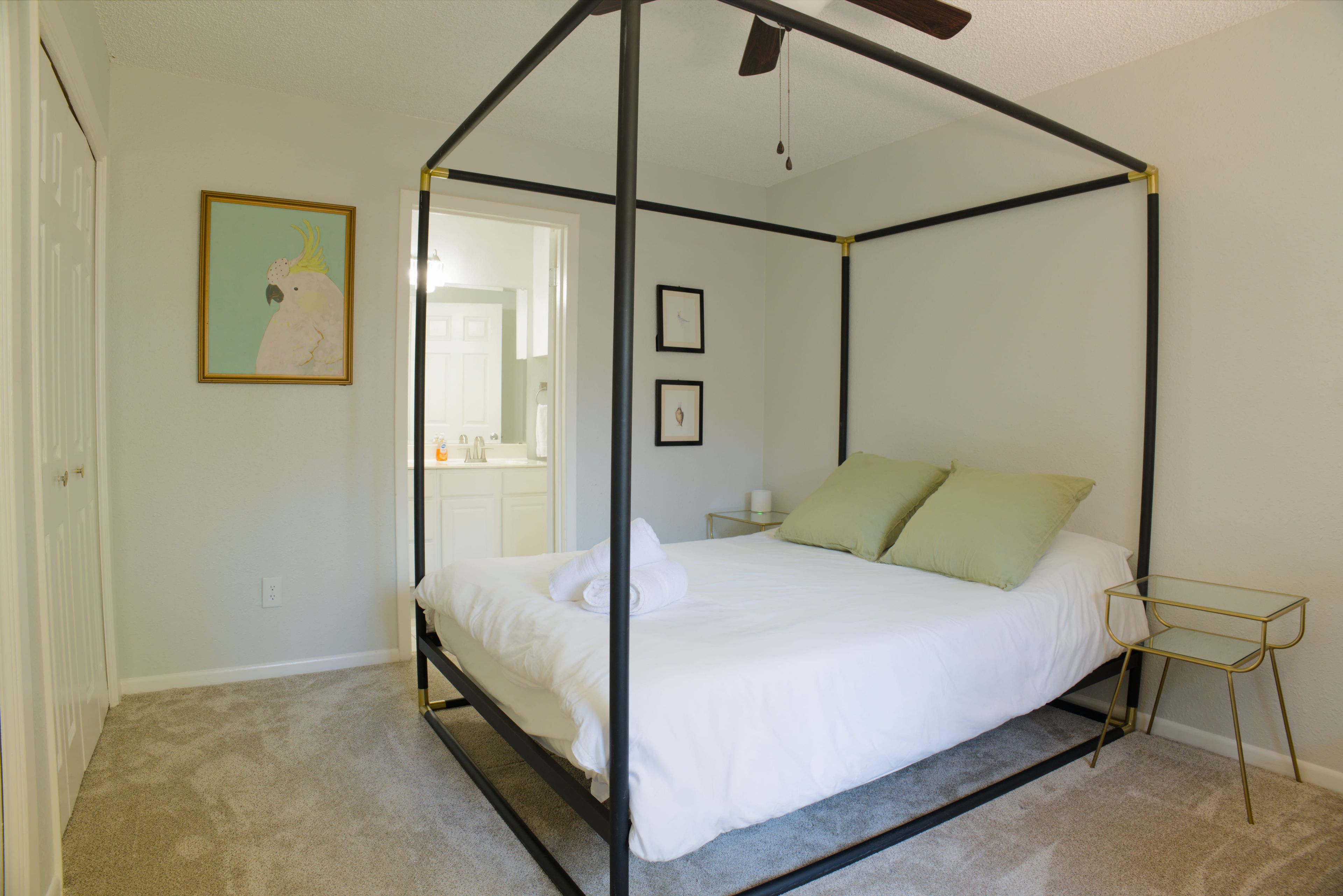 A four-poster canopy bed with white bedding, a small bedside table, and a framed picture on the wall.