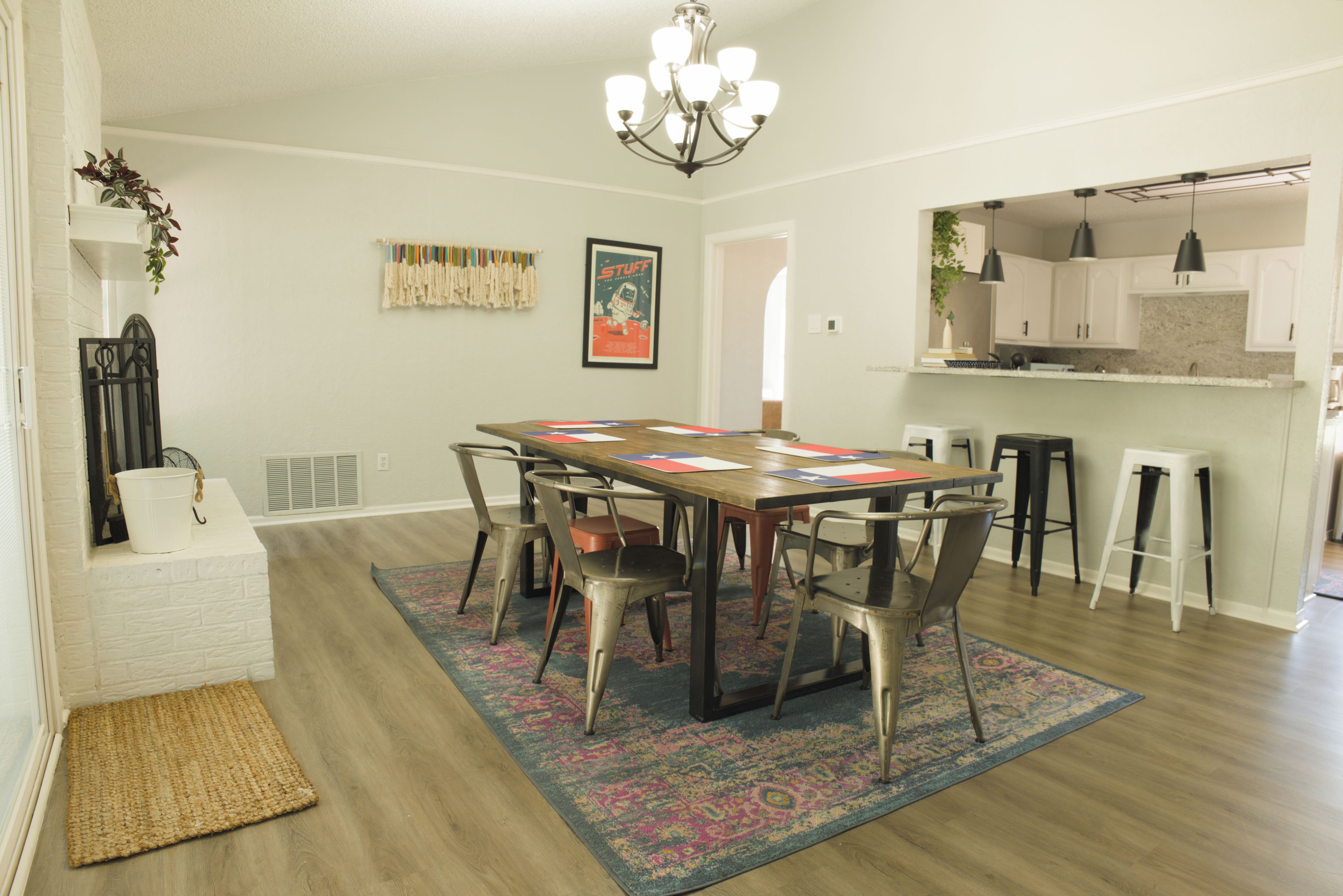 Un coin repas avec une table en bois, des chaises en métal, un tapis à motifs et un lustre.
