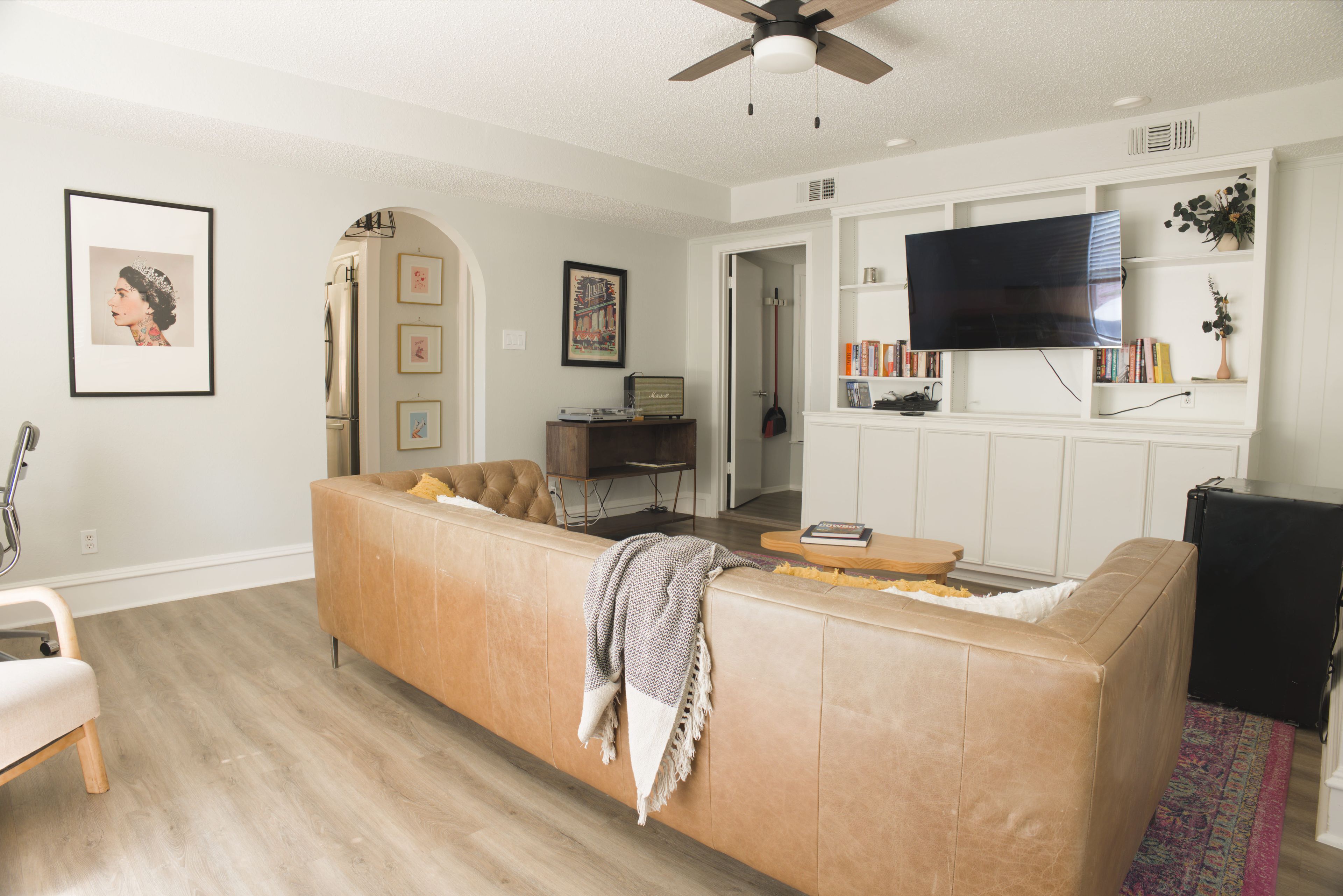 A living room with a beige sectional sofa, a flat-screen TV mounted on the wall, and a ceiling fan.