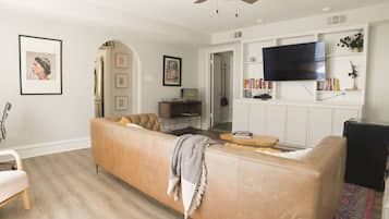 A living room with a beige sectional sofa, a flat-screen TV mounted on the wall, and a ceiling fan.