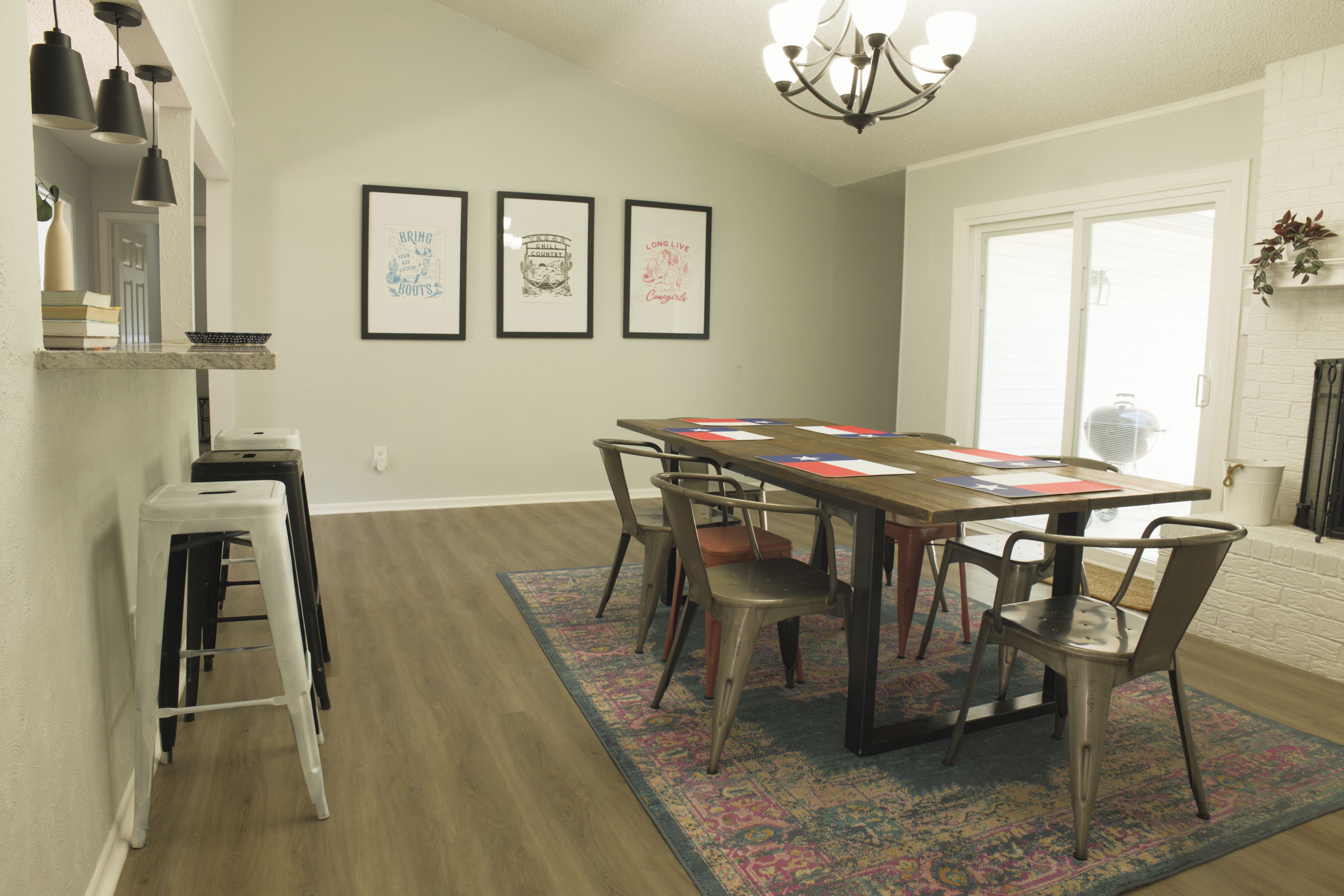 A dining area with a long table, chairs, a chandelier, and framed pictures on the wall.
