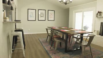 A dining area with a long table, chairs, a chandelier, and framed pictures on the wall.